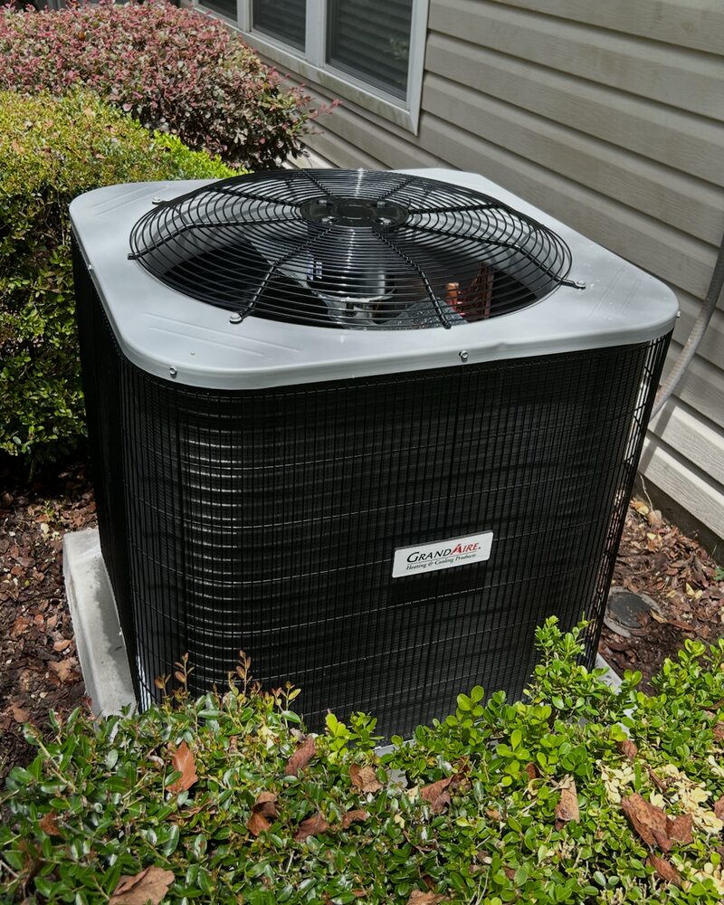 Outdoor AC condenser installed in tidy landscaping beside a home